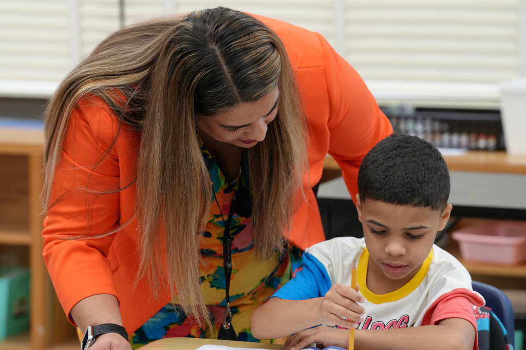 Principal Jovana Williams leans over a classroom table helping two students with their work.