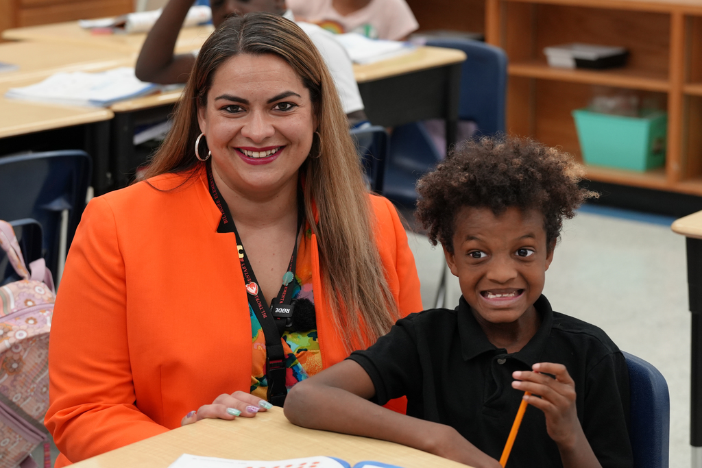 Principal Jovana Williams smiles while sitting with two students in her classroom.