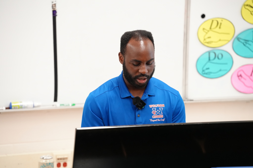 Chorus Teacher Cyriac Adjevi leading students in a singing exercise, with choir members smiling and engaging in the classroom.