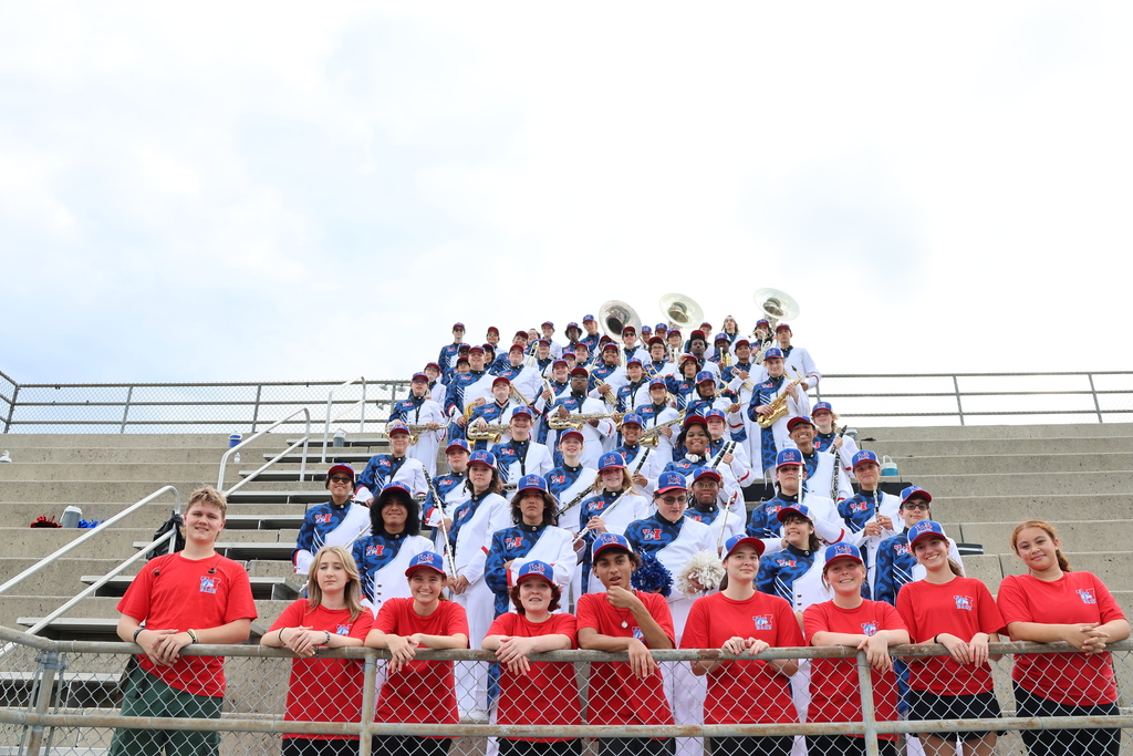 A group of Wolfson High School band students performing on stage, playing brass and woodwind instruments under bright stage lights.