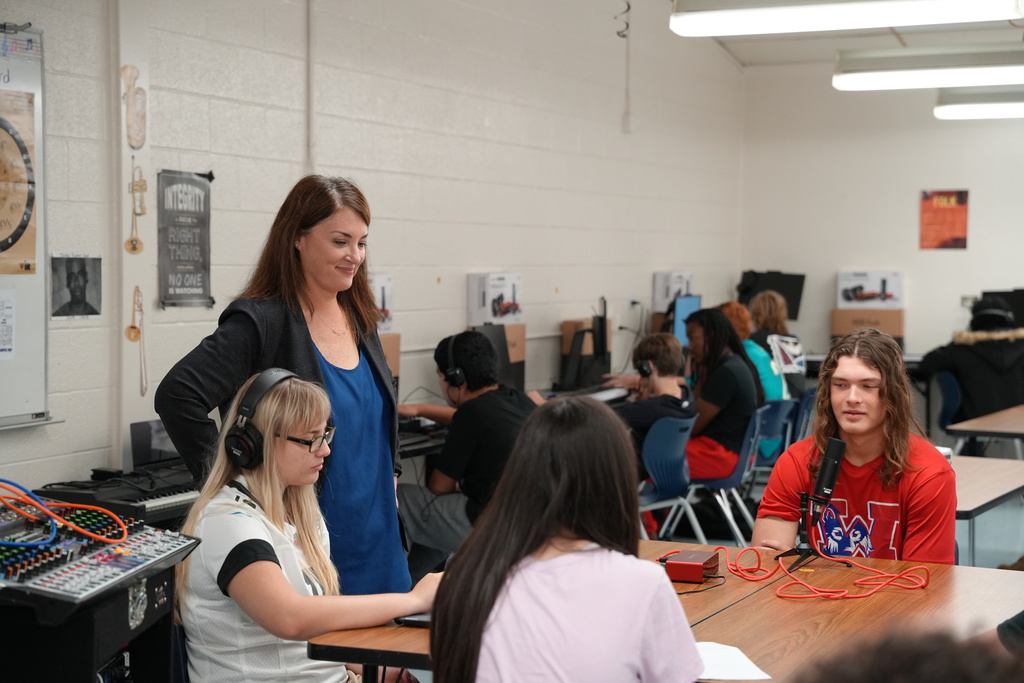 Band Director Kristina Ledford working with students in the music room, offering guidance as students practice with a podcast.