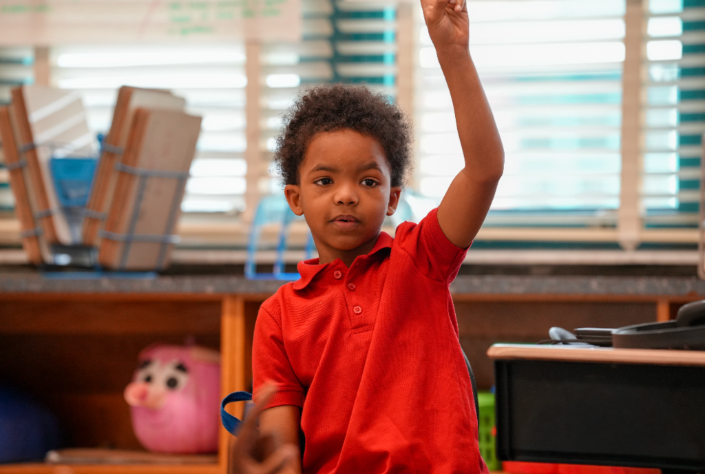 Angie Collins leans over a student’s desk, guiding them through a classroom activity with encouragement and care.