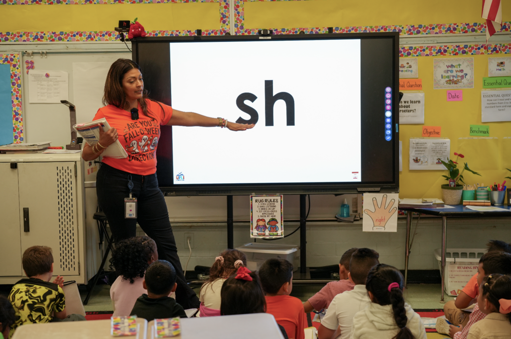 Abneris Howard stands at the front of her classroom, engaging students with a lively reading activity on the whiteboard.