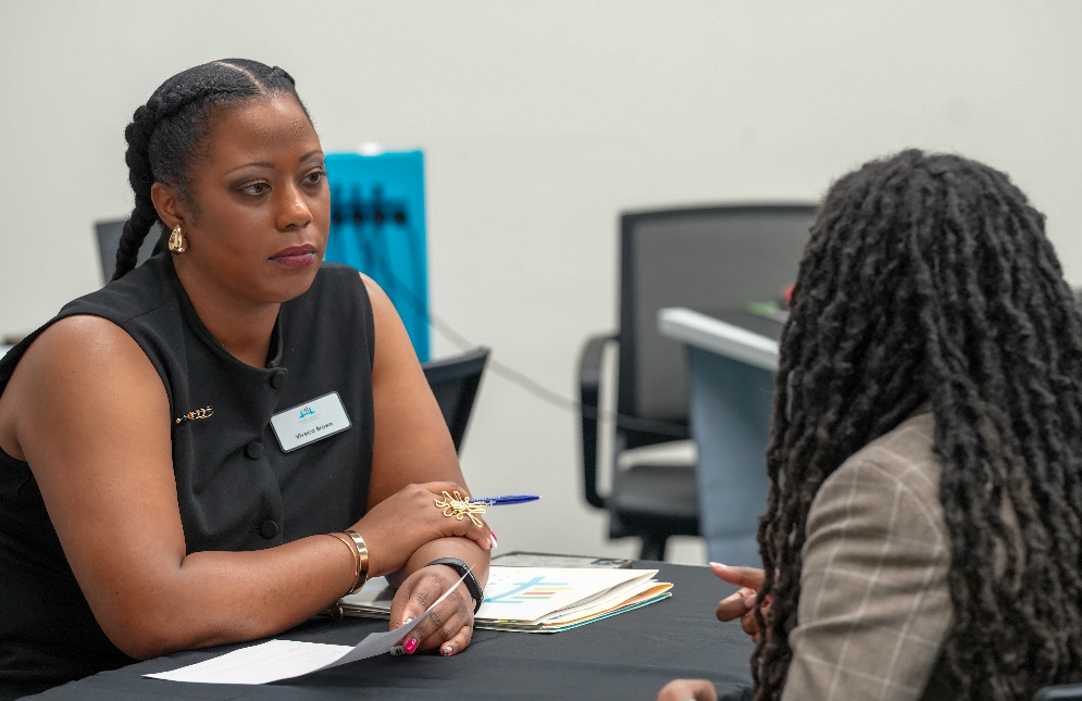  A candidate speaks with a DCPS recruiter at a table during the Retired Educators Hiring Fair, with others meeting in the background.