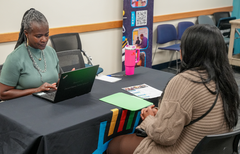  A candidate speaks with a DCPS recruiter at a table during the Retired Educators Hiring Fair, with others meeting in the background.