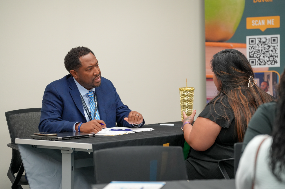  A candidate speaks with a DCPS recruiter at a table during the Retired Educators Hiring Fair, with others meeting in the background.