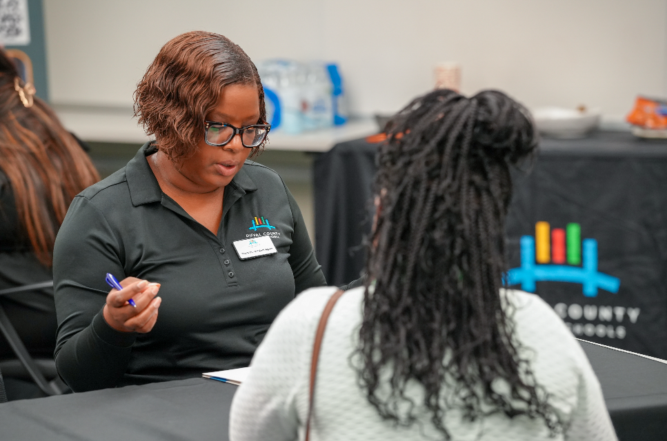  A candidate speaks with a DCPS recruiter at a table during the Retired Educators Hiring Fair, with others meeting in the background.