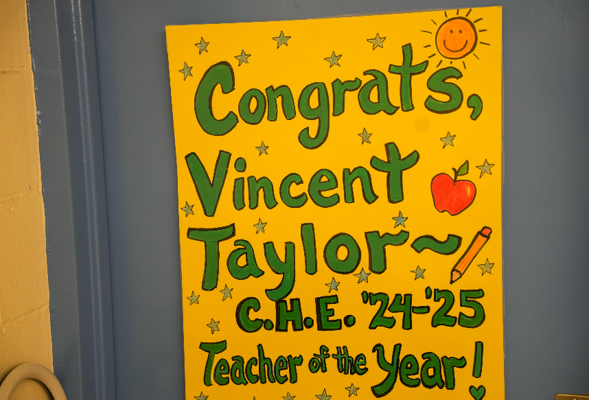 A bright yellow handmade poster on a classroom door that reads “Congrats, Vincent Taylor — C.H.E. ’24–’25 Teacher of the Year!” decorated with stars, a red apple, and a smiling sun.