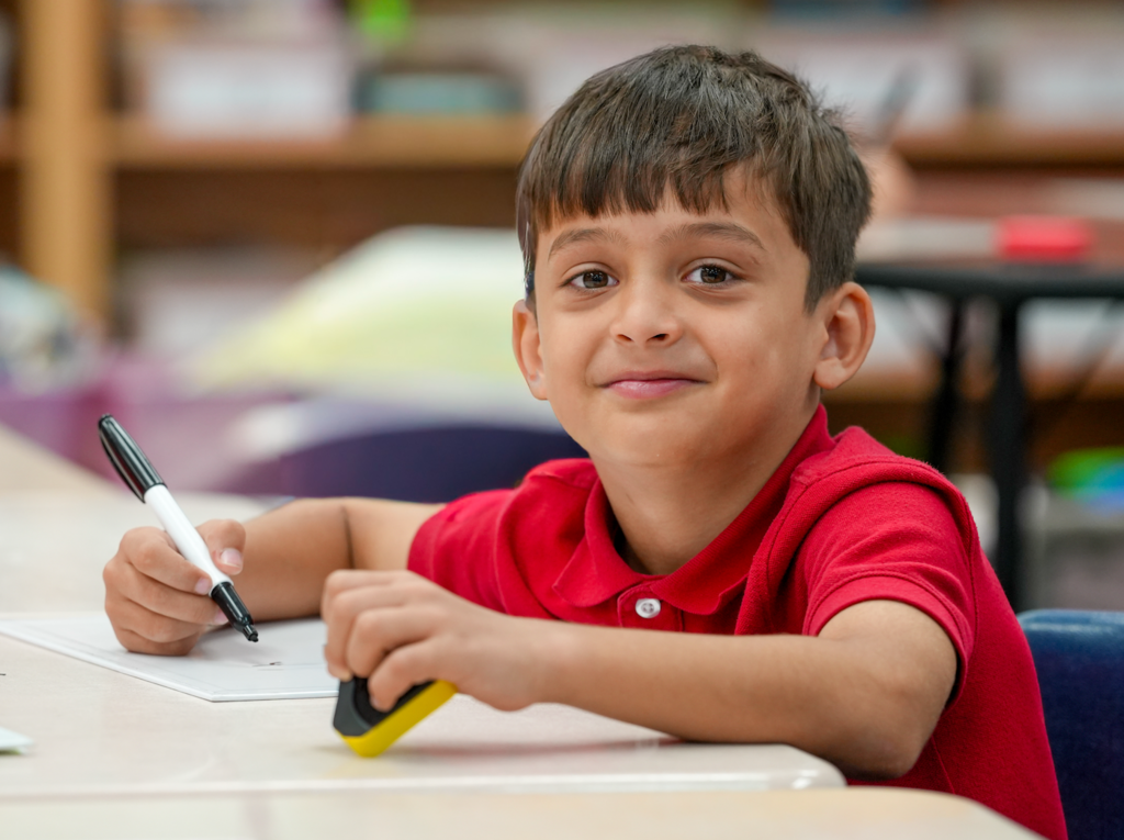 Elementary students in a classroom smiling while working at a table.