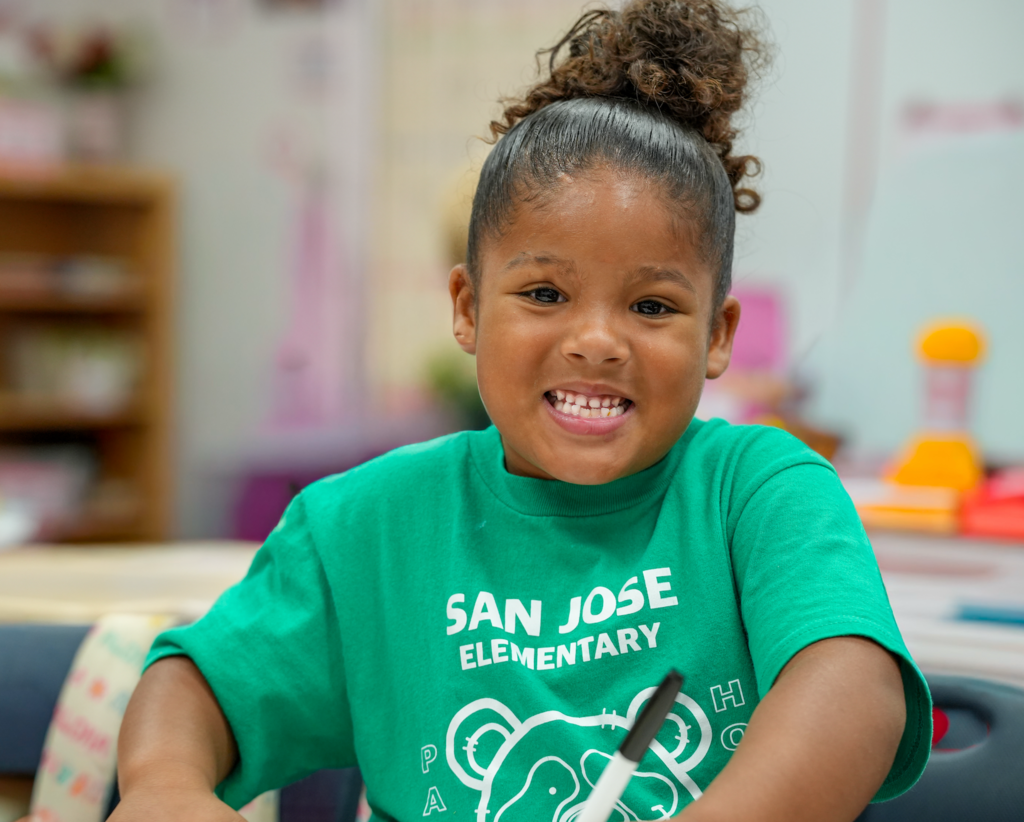 Elementary students in a classroom smiling while working at a table.