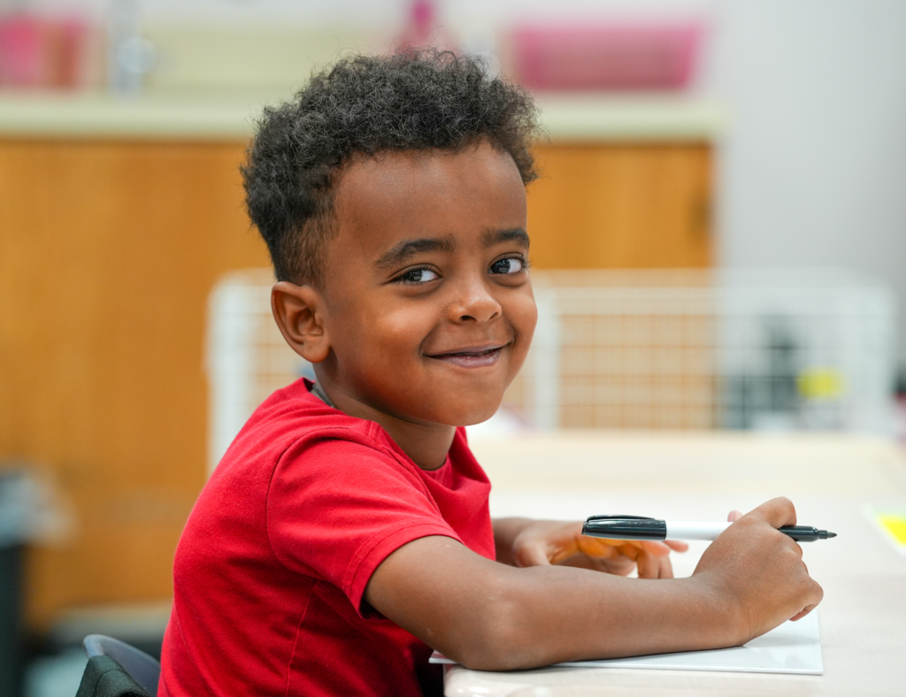 Elementary students in a classroom smiling while working at a table.