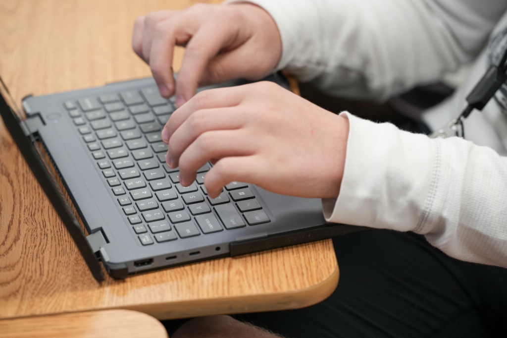 Close-up of hands typing on a laptop during class instruction.