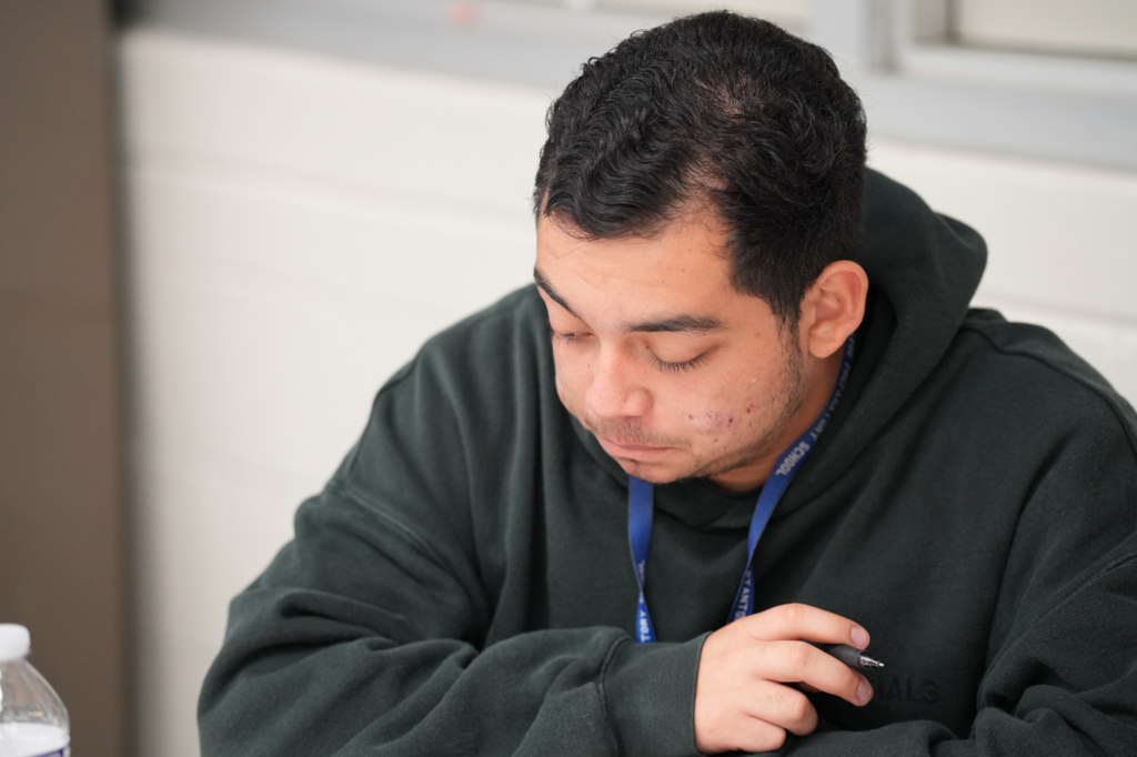 A student focuses on classwork as Norma Crespo-Lowery observes nearby, offering guidance and support in the classroom.