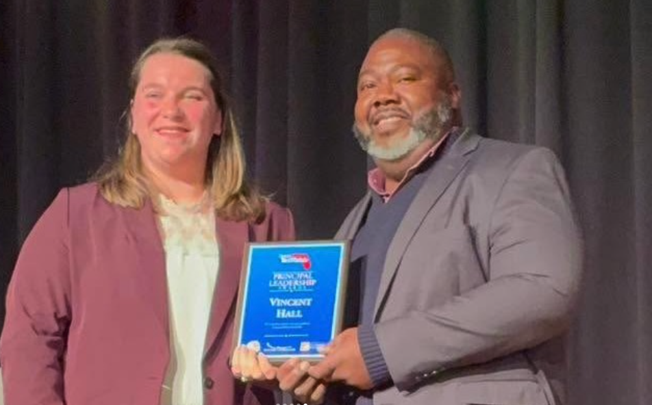 Florida TaxWatch representative presents the Principal Leadership Award to Principal Hall on stage at William M. Raines High School.