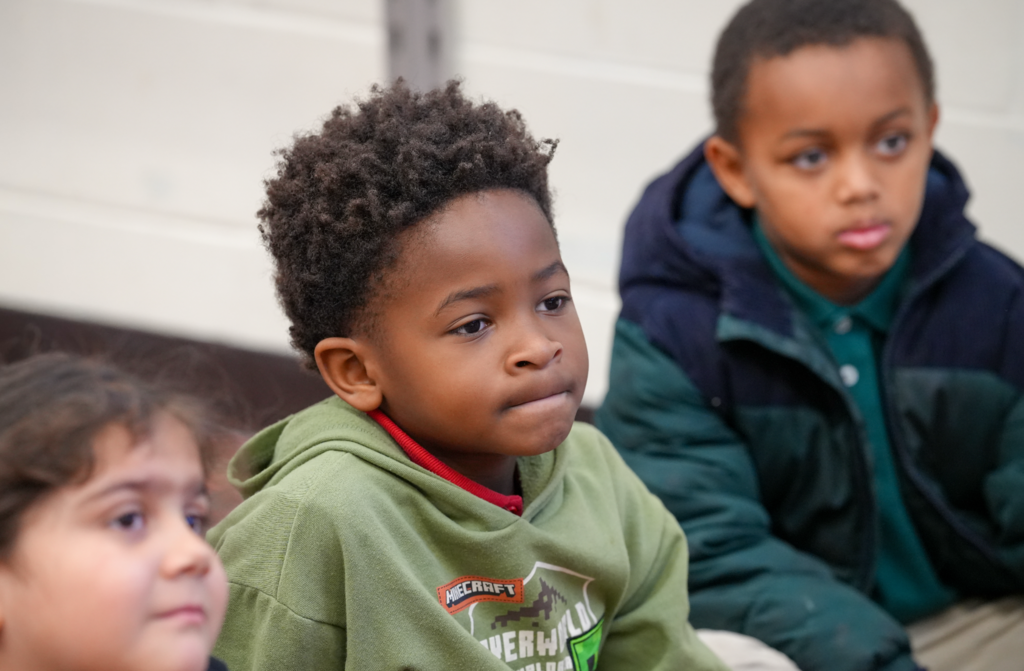 A student sits at a desk listening attentively during a classroom reading session.