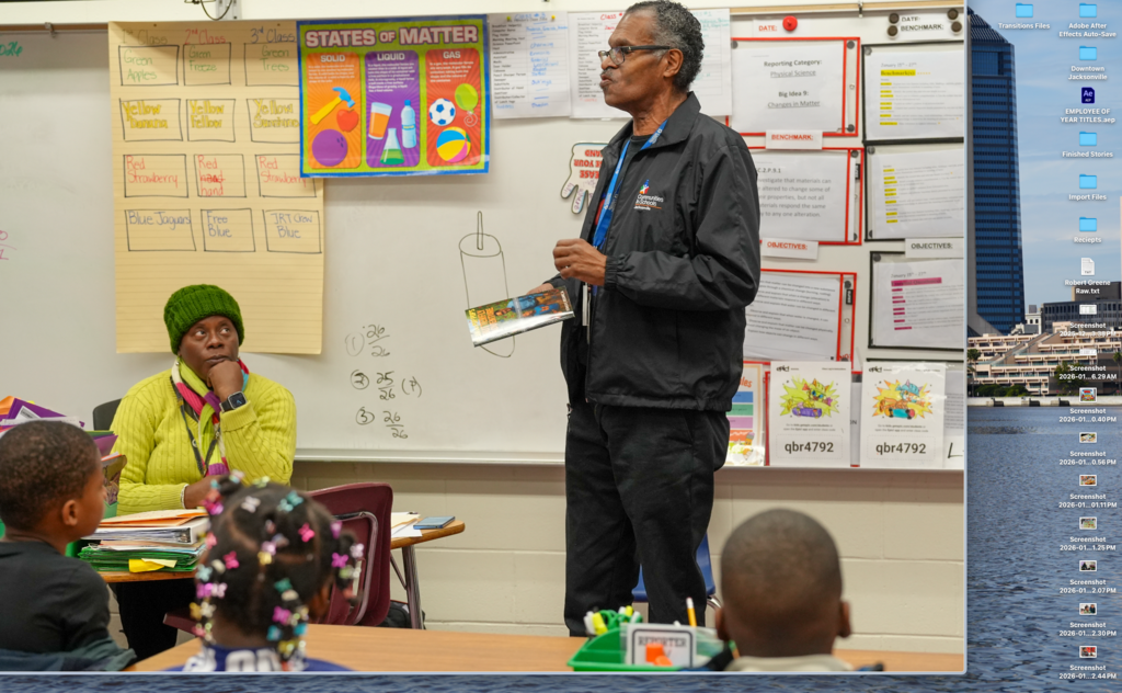 A community volunteer reads a book aloud to a group of students seated around a table during the Real Men Read literacy event.
