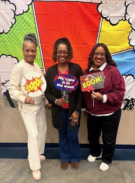 Three counselors hold up signs with superhero verbiage and smile at the camera.