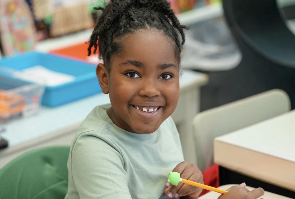 A smiling student sits in Elizabeth Dent’s classroom with learning materials behind them.