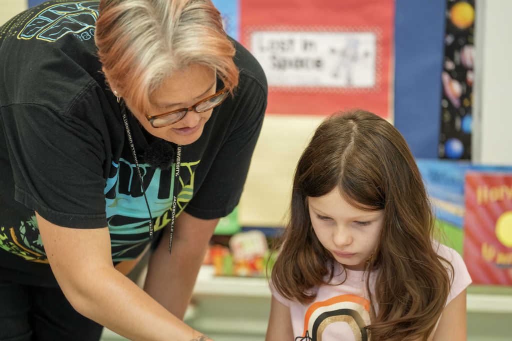 Elizabeth Dent sits beside a student and listens as they talk in the classroom.