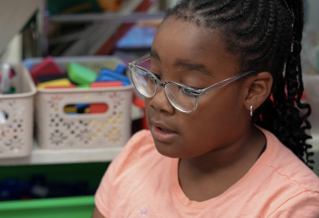 A student wearing glasses sits at a desk inside Elizabeth Dent’s classroom.