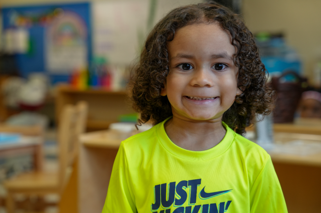 Young student seated at a table, smiling during Montessori classroom activity.