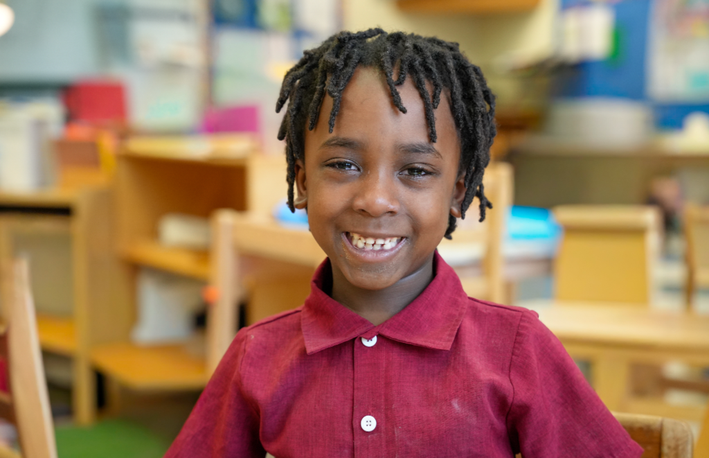 Student in a red shirt smiling during hands-on classroom learning.
