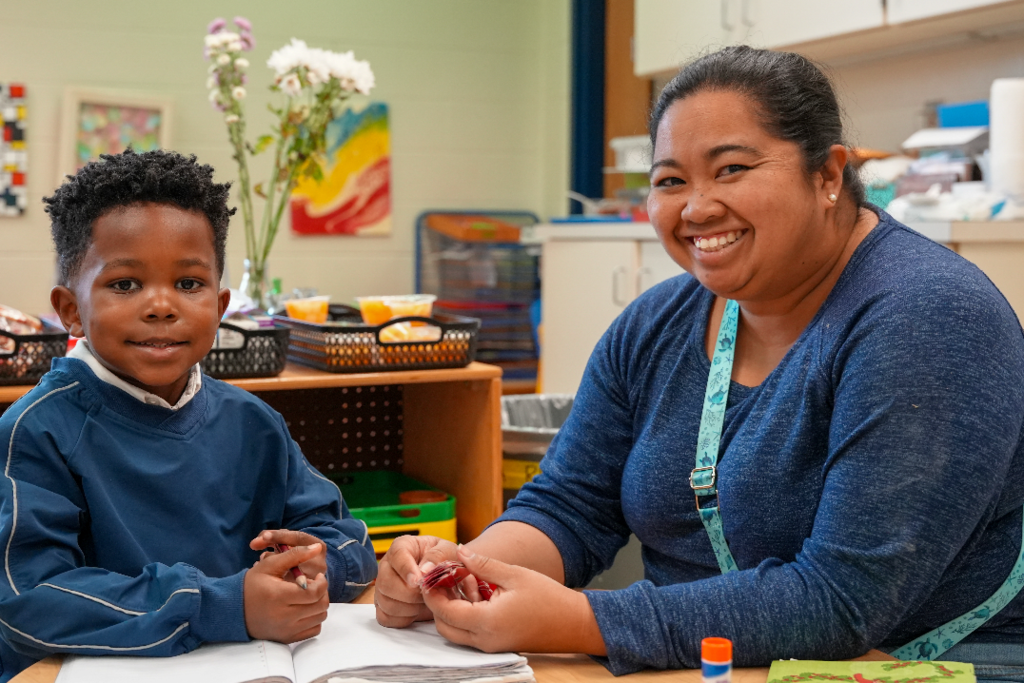 Erika Cunaamay assisting a young student with Montessori learning materials at a classroom table.