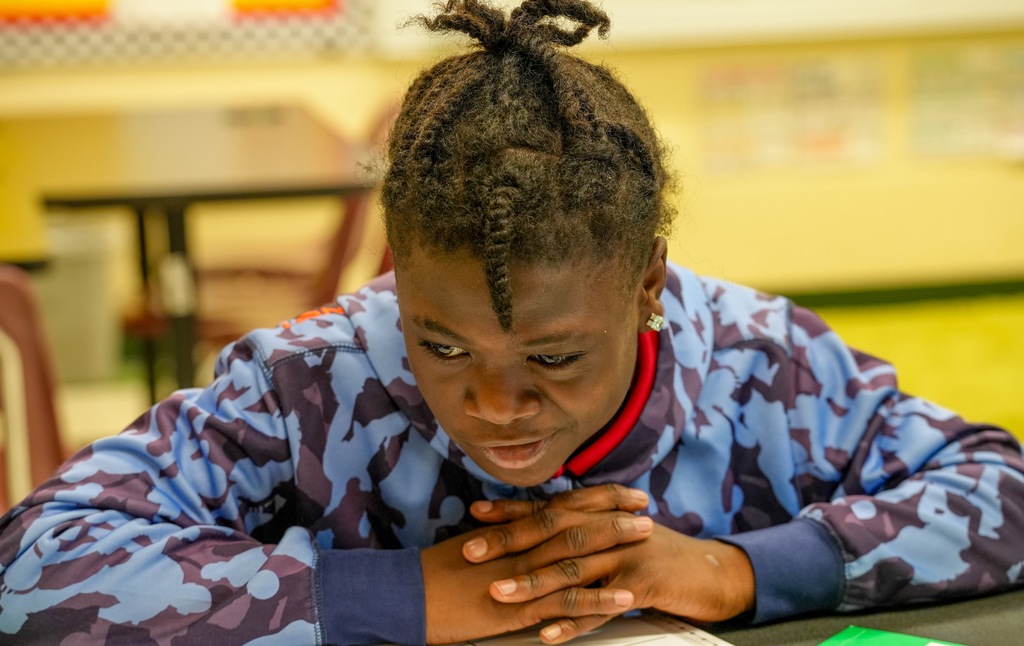 A student leans forward with focused expression while working on a math problem in Benton Jones’ classroom.