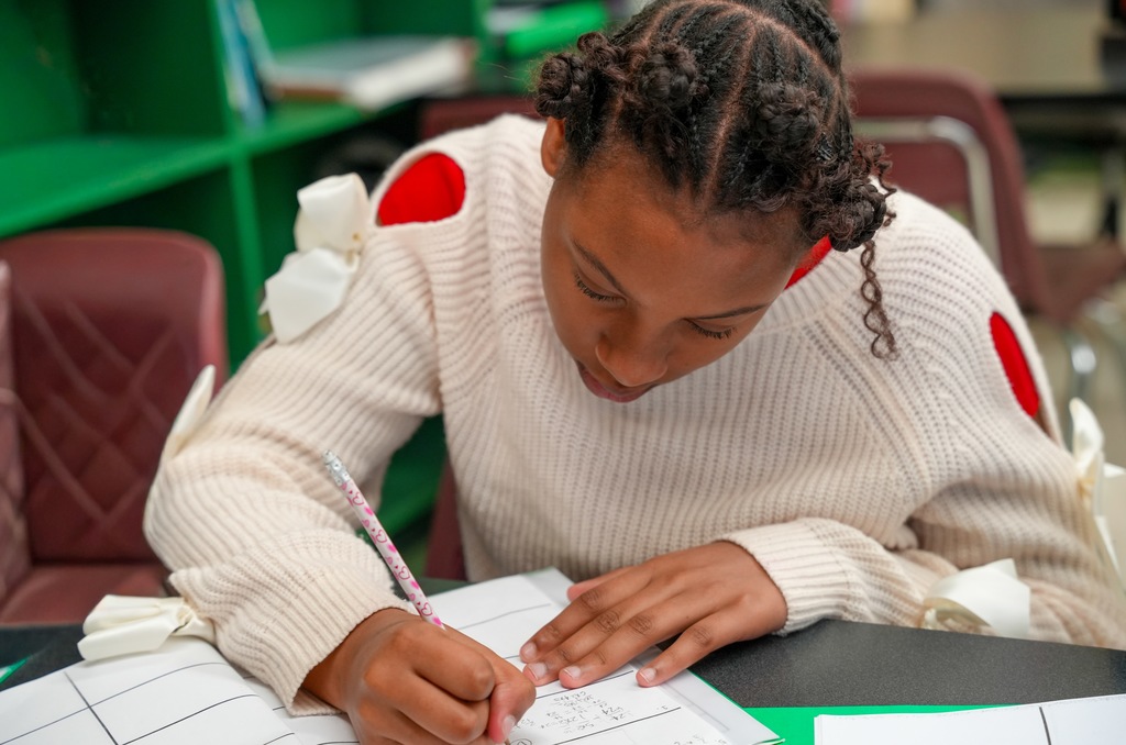 A student carefully writes math calculations in her workbook during instruction with Benton Jones.