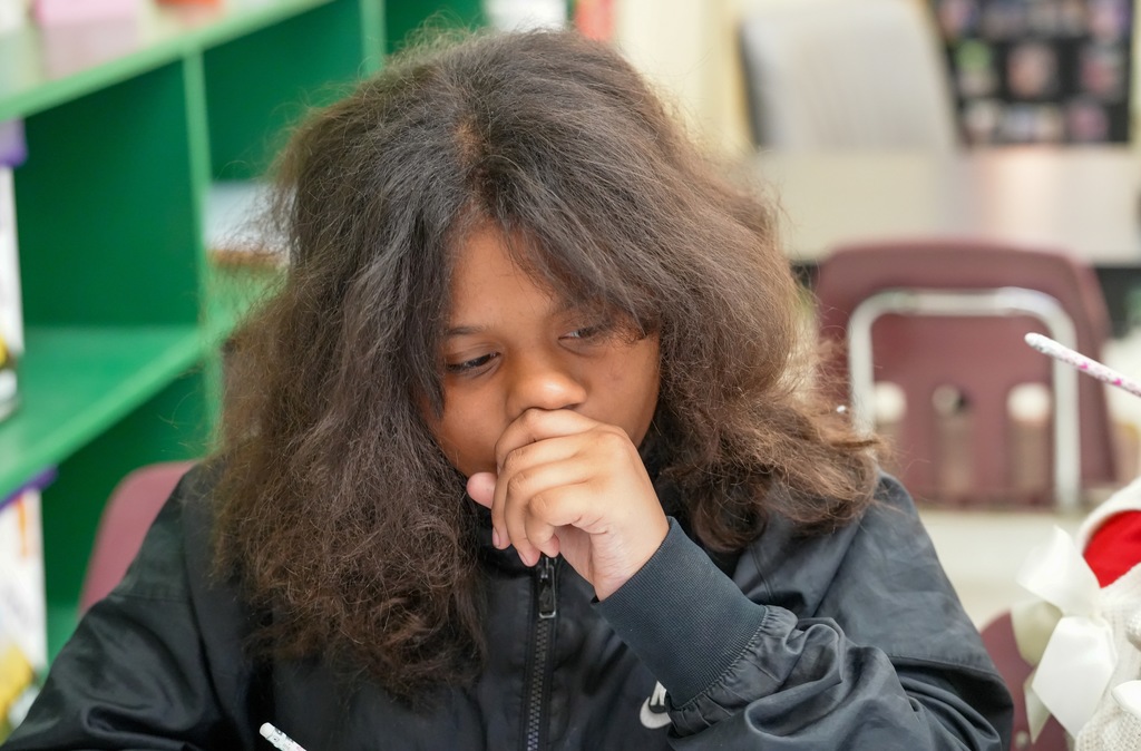 A student concentrates on her math worksheet, hand partially covering her mouth as she thinks during class with Benton Jones.