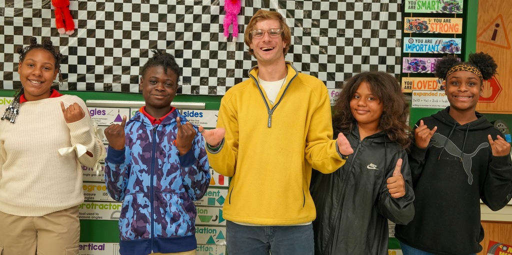 Benton Jones stands smiling with four students in his classroom at Fort Caroline Elementary School, posing together in front of a math display wall.