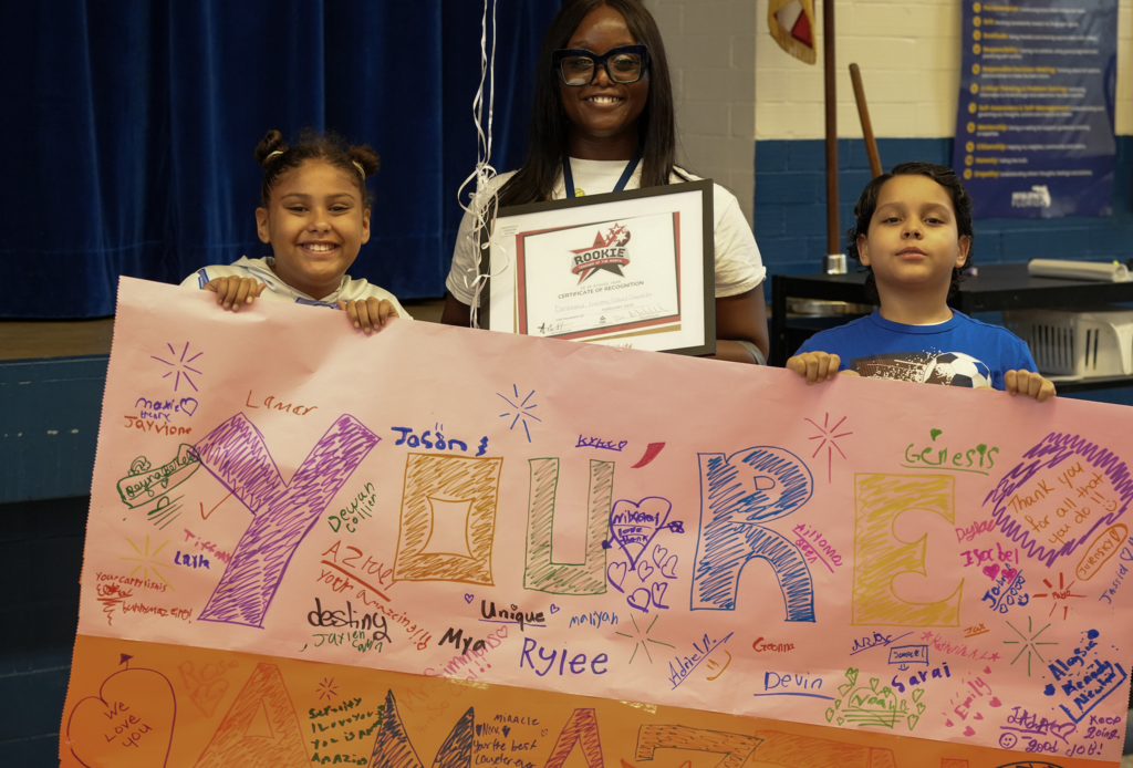 Mrs. Dankeshia Ivester smiles while holding a large congratulatory poster, surrounded by students and staff during her Rookie Counselor of the Month recognition presentation.