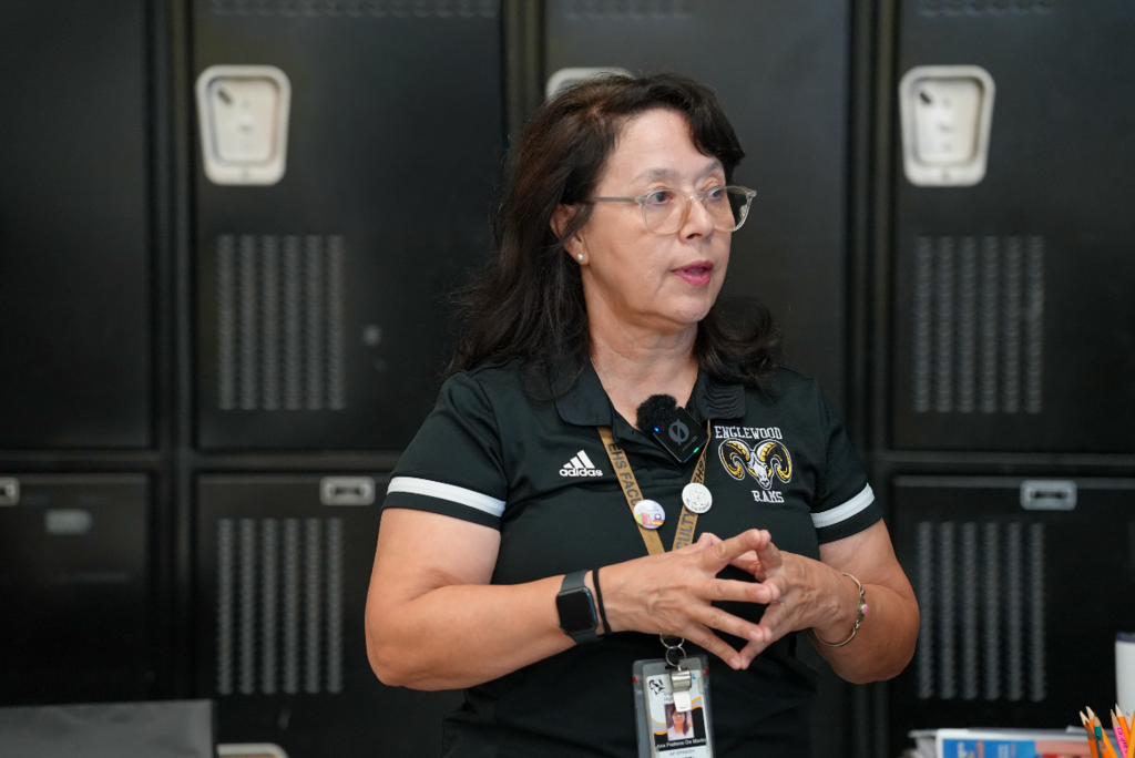 Señora Martin gestures with her hands while teaching, standing confidently in front of classroom lockers at Englewood High School.