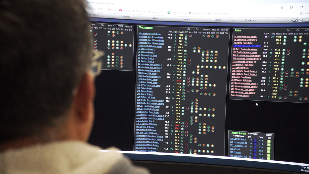 A close up of a computer screen with data. In the foreground is the back of the head of a maintenance worker watching the screen.
