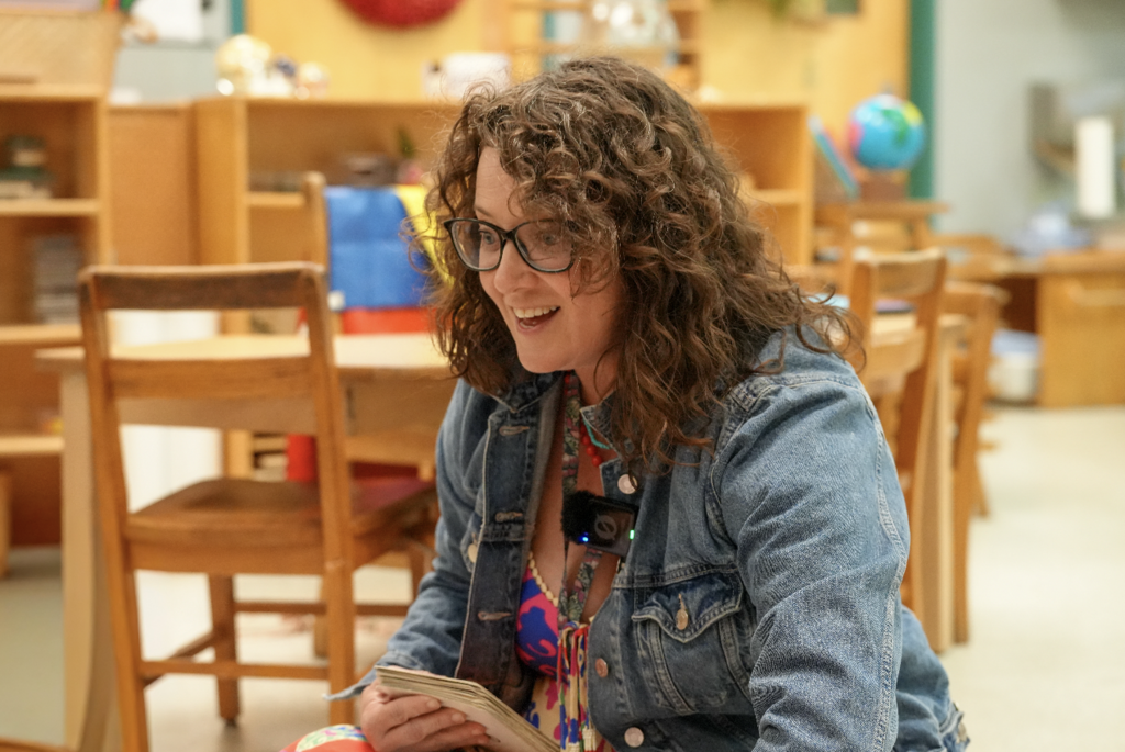 Shannon Simon kneels beside a student, guiding them through a hands-on Montessori learning activity.