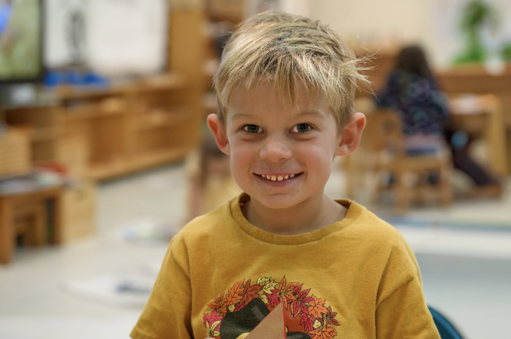 Two elementary students stand together in the classroom smiling during their Montessori work period.