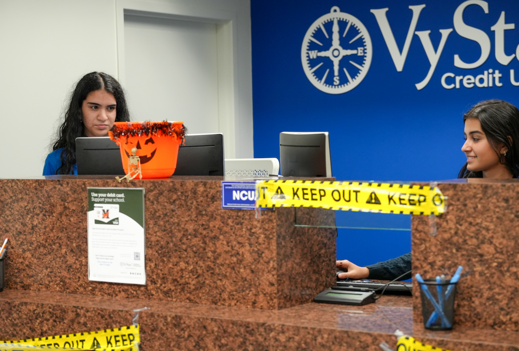 Student working at a computer behind a credit union counter, focused on a transaction.