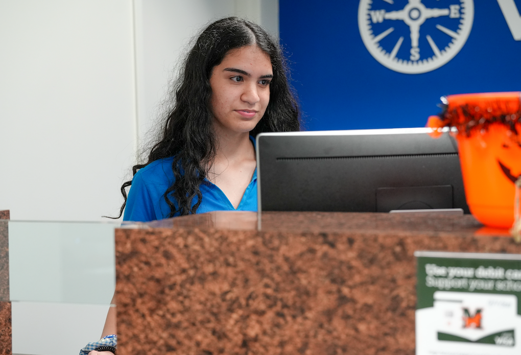 Student in a blue shirt listening during a customer interaction.