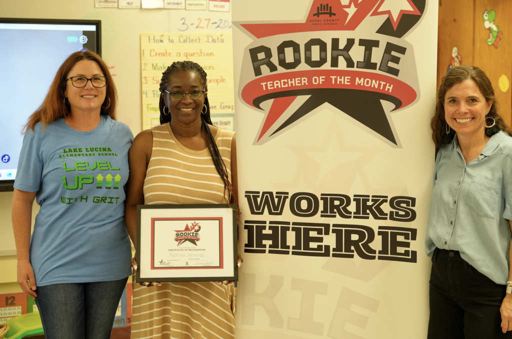 Katrina Jennings poses with her certificate beside a large “Rookie Teacher of the Month Works Here” banner inside her classroom.