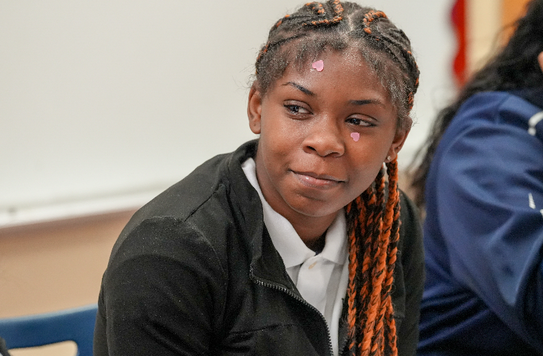 Student turned slightly, listening and engaged with peers in Randolph Myrie’s classroom