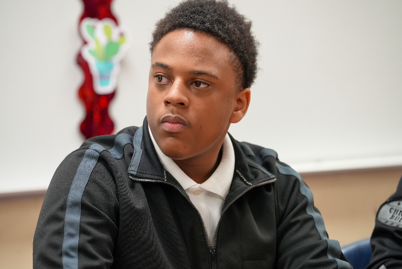 Student turned slightly, listening and engaged with peers in Randolph Myrie’s classroom