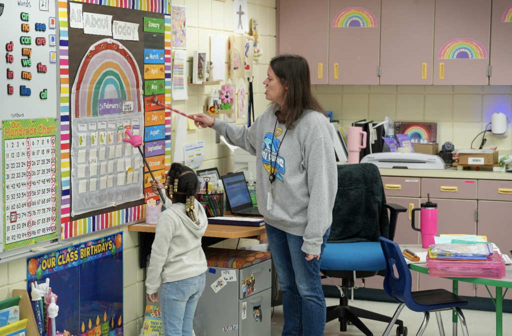 Brittany Barbatelli working one-on-one with a young student at a classroom table surrounded by colorful learning materials.