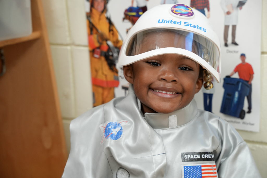 Young student wearing a play helmet and smiling during a classroom activity.