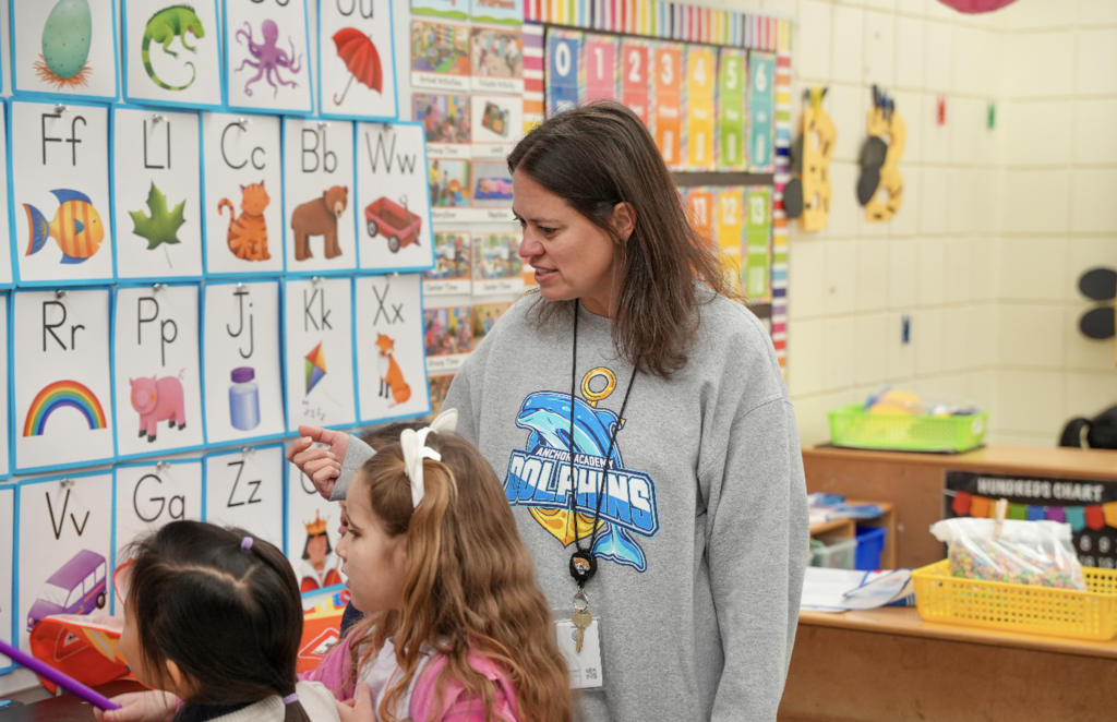 Brittany Barbatelli kneeling beside students and assisting with a hands-on classroom activity.