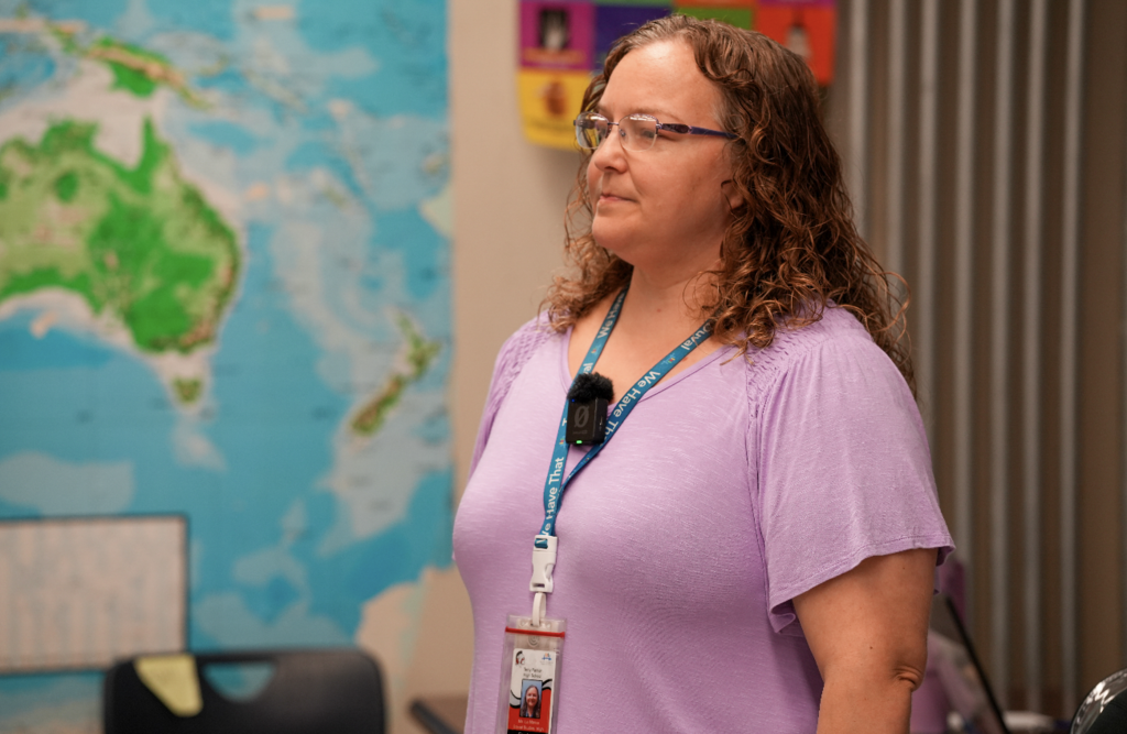 Rebecca LaMance, wearing a purple top, stands near a classroom map while teaching.