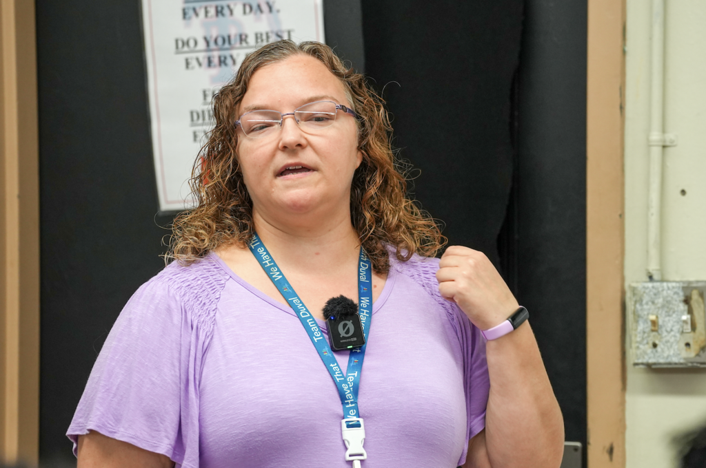 Rebecca LaMance, wearing a purple top, speaks to students while standing at the front of the classroom.