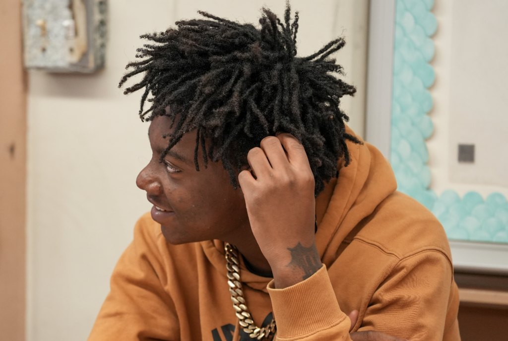A student with curly hair rests their head on their hand while working at their desk.
