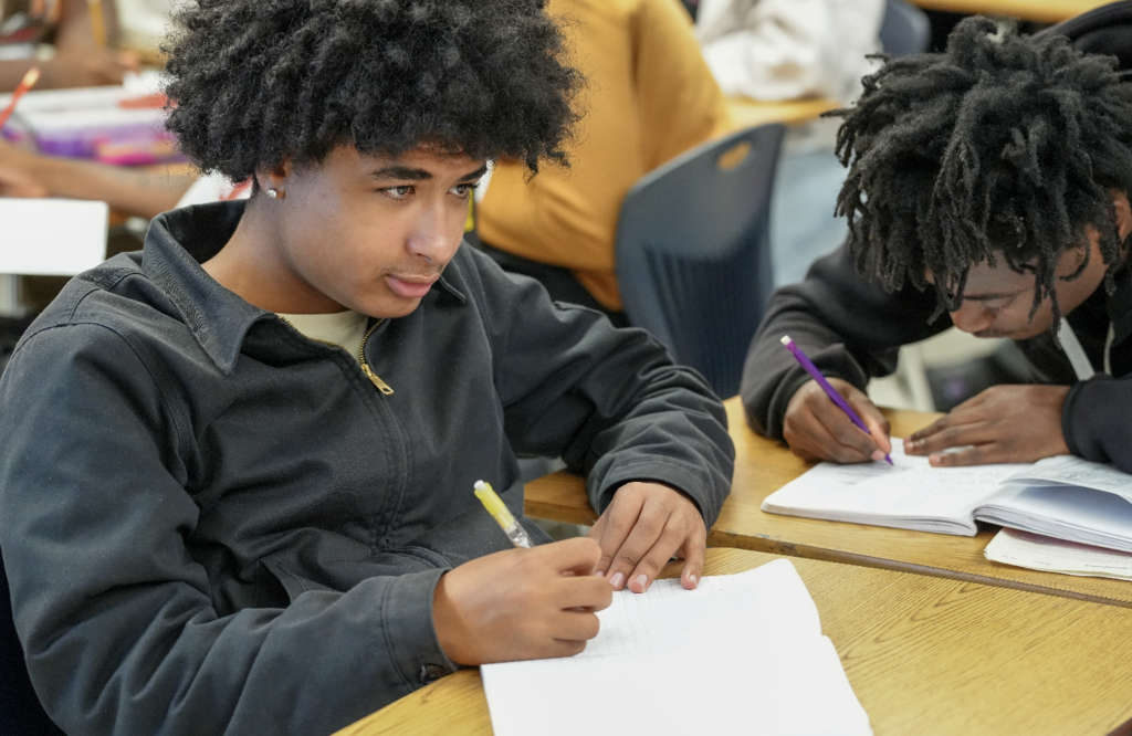 A student writes in a notebook, focused on a classroom assignment.