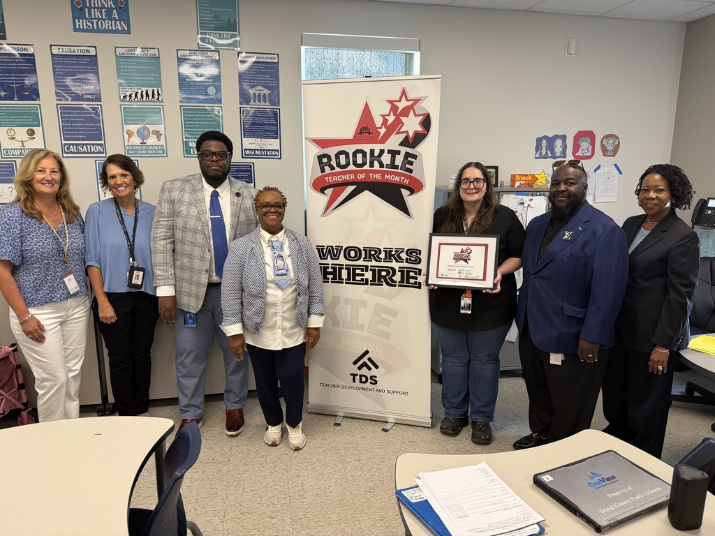 Amanda Duckworth stands next to a colleague holding her Rookie Teacher of the Month certificate in a classroom.