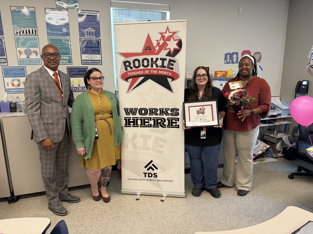 Amanda Duckworth stands next to a colleague holding her Rookie Teacher of the Month certificate in a classroom.